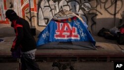 FILE - A man walks past a homeless encampment in downtown Los Angeles, Oct. 25, 2023. 
