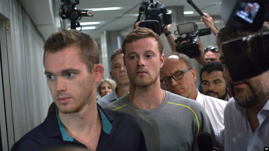 Journalists surround American Olympic swimmers Gunnar Bentz, left, and Jack Conger, center, as they leave the police station at Rio International airport early Aug. 18, 2016. 