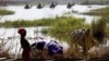 FILE - Men on camels cross the water as a woman washes clothes in Lake Chad at Ngouboua.
