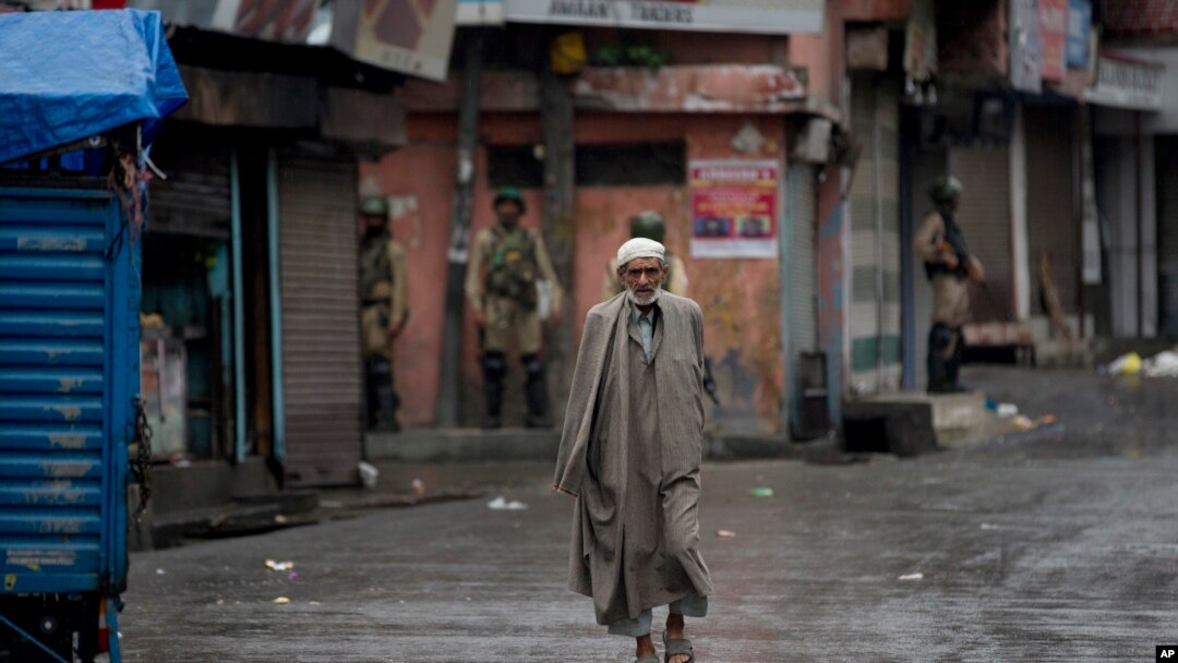A Kashmiri man walks as Indian paramilitary soldiers stand guard during security lockdown in Srinagar, Indian controlled Kashmir, Wednesday, Aug. 14, 2019.