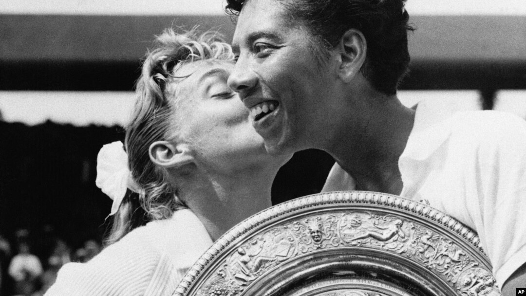 Althea Gibson holds the Wimbledon women's singles trophy as she gets a kiss from Darlene Hard, whom she defeated at Wimbledon in England in this July 6, 1957 file photo. 