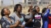 Women from a group of churchgoers wail at the site, Sunday Aug. 19, 2012 at the Lonmin platinum mine, background, near Rustenburg, South Africa, during a memorial service for 34 dead striking miners who were shot and killed by police last Thursday.