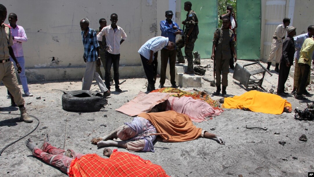 Somalis stand next to the bodies of civilians who were killed in a car bomb attack on a restaurant in Mogadishu, April 5, 2017.