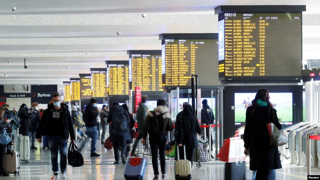 People walk carrying their luggage past train schedule displays at Termini train station, on the day the government lays out a plan of coronavirus disease (COVID-19) restrictions over the Christmas period, in Rome, Dec. 19, 2020. 