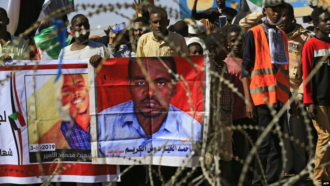 Sudanese protesters rally in front of a court in Omdurman near the capital Khartoum, Dec. 30, 2019, during the trial of intelligence agents for the death of teacher Ahmed Al-Khair, portrait at right, while in custody of intelligence services. 