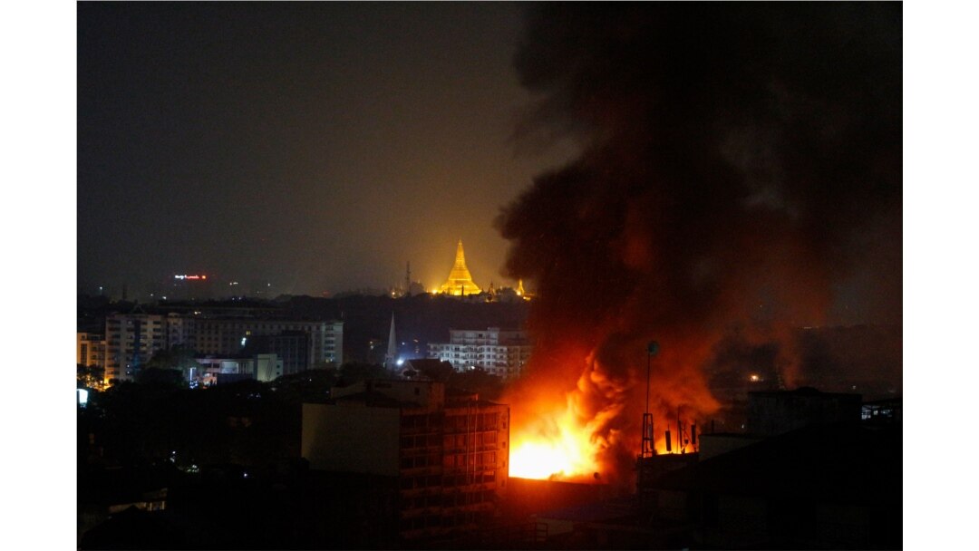 Smoke rises from a fire at Ruby Mart in Yangon in the early morning of April 1, 2021 with the Shwedagon Pagoda seen illuminated in the background, as the country continues to be in turmoil after the February military coup. (Photo by STR / AFP)