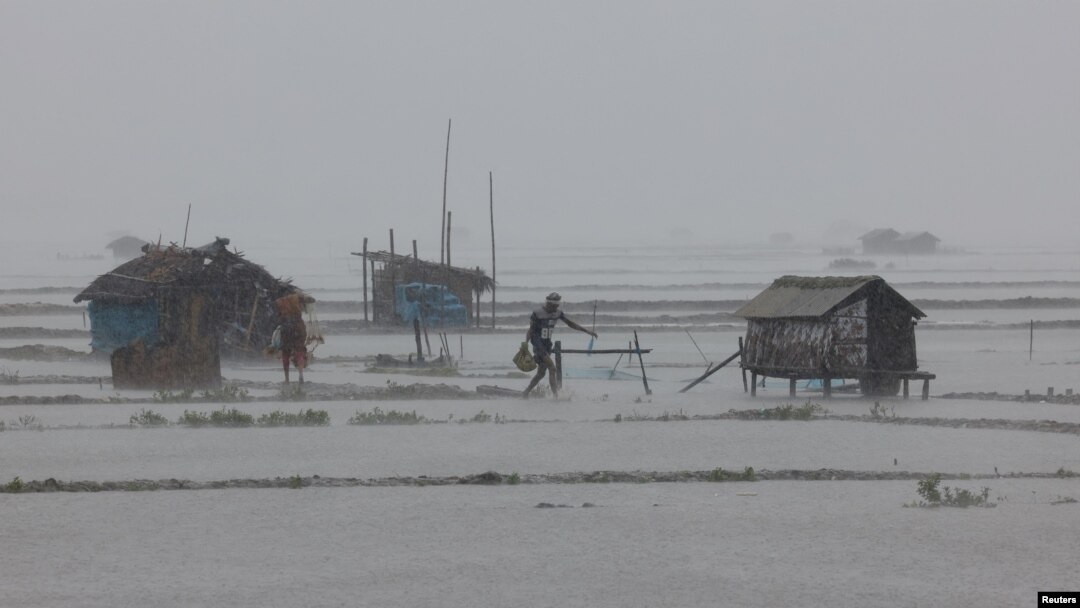 People walk along shrimp and crab farms that are flooded due to heavy rain as Cyclone Remal passes the country, in the Shyamnagar area of Satkhira, Bangladesh, May 27, 2024.