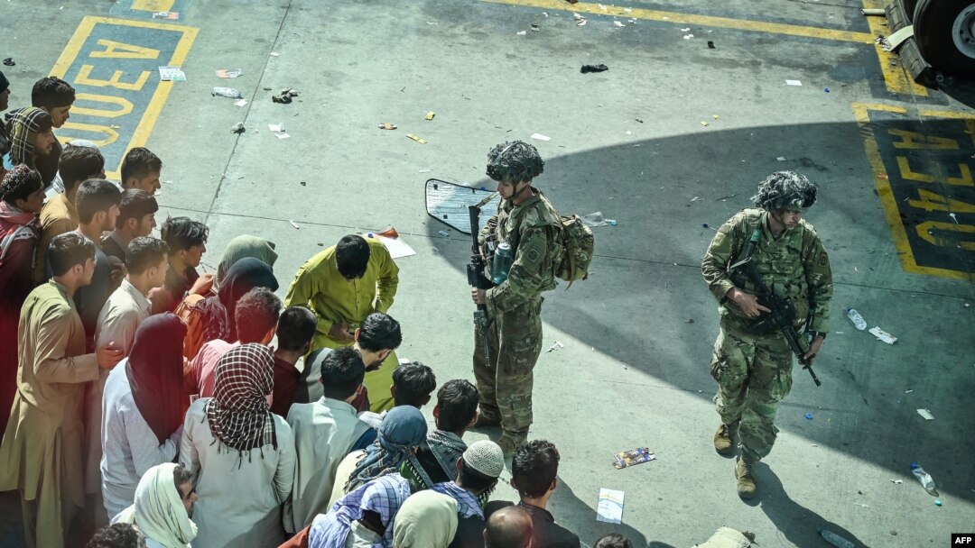 US soldiers stand guard as Afghan people wait at the Kabul airport in Kabul on August 16, 2021, after a stunningly swift end to Afghanistan's 20-year war, as thousands of people mobbed the city's airport trying to flee the group's feared hardline brand…