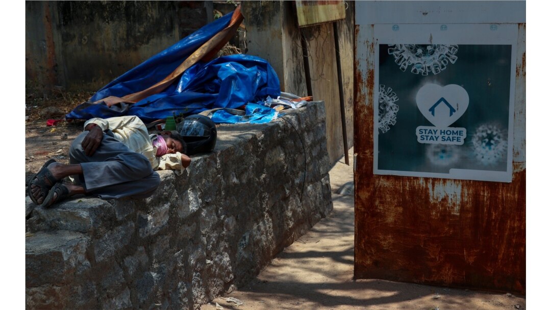 An Indian man sleeps next to a sign urging people to stay at home as a precaution against coronavirus in the premises of a hospital in Hyderabad, India, April 29, 2021.