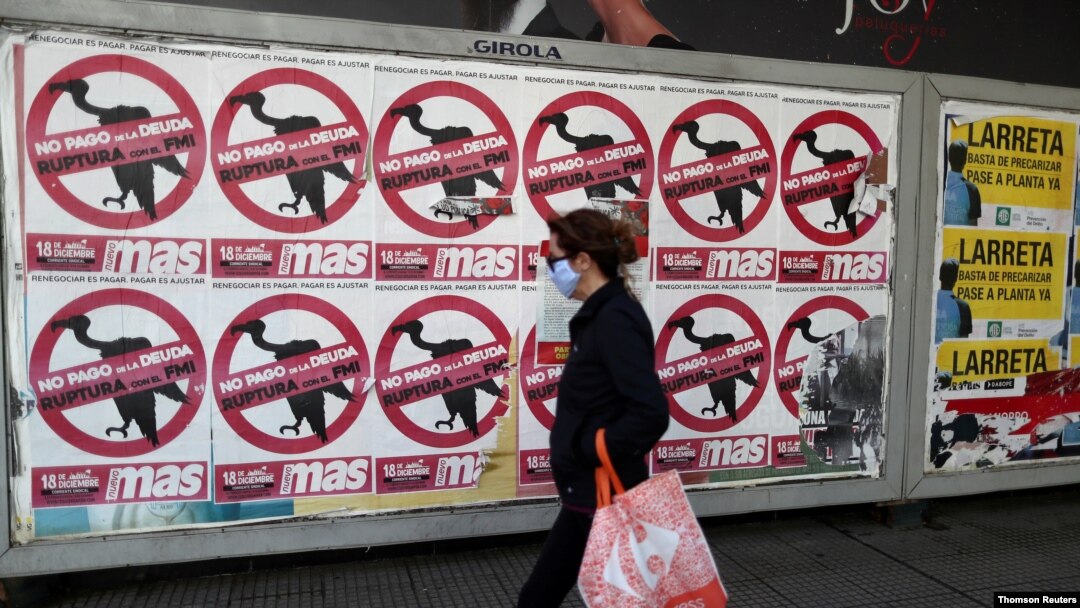 FILE - A pedestrian wearing a face mask as a preventive measure against the coronavirus walks past posters on the street that read 'No to the payment of the debt. Break with the IMF' in Buenos Aires, Argentina, May 27, 2020.