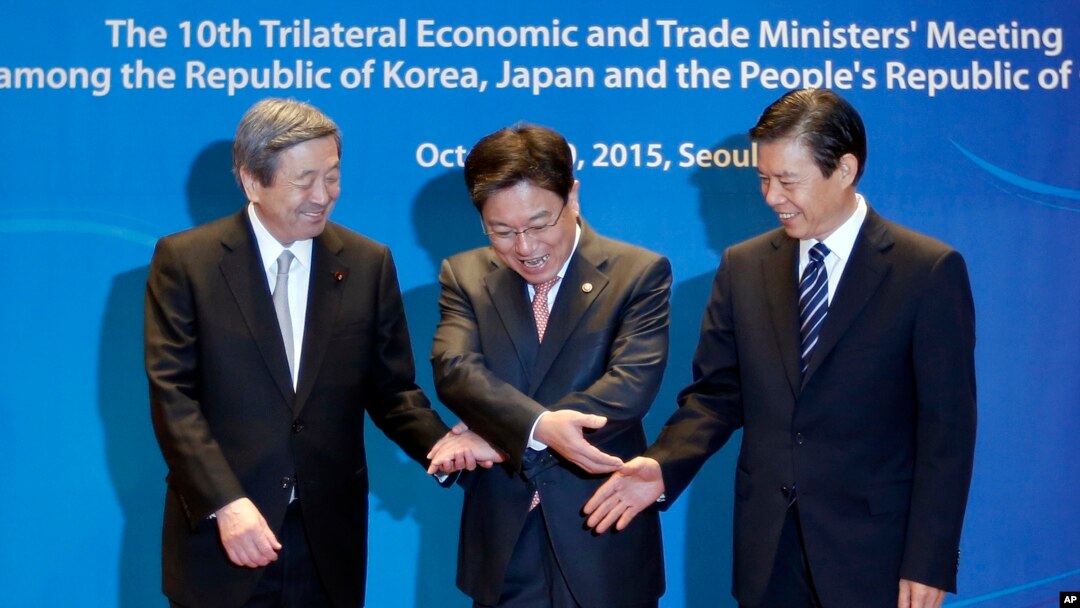 South Korea's Trade, Industry and Energy Minister Yoon Sang-jick, center, tries to hold hands to pose for the media with Japan's Economy, Trade and Industry Minister Motoo Hayashi, left, and China International Trade Representative Zhong Shan before the 1