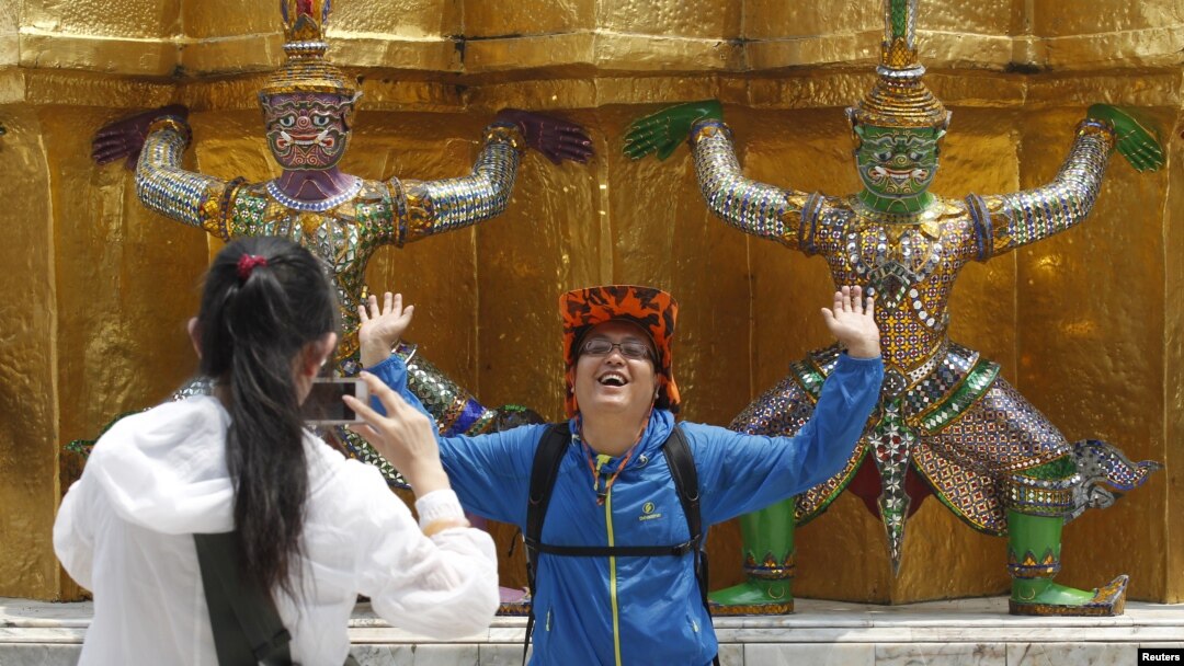 FILE - A Chinese tourist strikes a similar pose to statues as they visit the Grand Palace in Bangkok, March 23, 2015. 