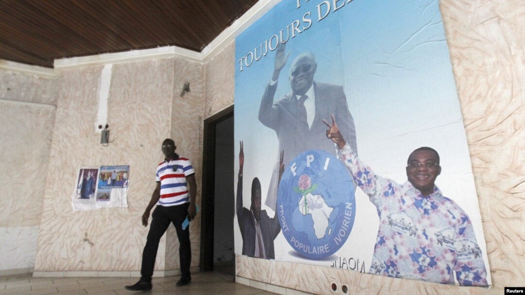 A man walks near a poster showing portraits of former Ivory coast president Laurent Gbagbo (C) and Former Ivory Coast prime minister Pascal Affi N'Guessan (R), leader of Ivorian Popular Front (FPI) at the FPI headquarters in Abidjan, September 2, 2015.